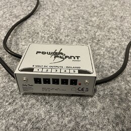 Stříbrný napájecí adaptér s nápisem POWER PLANT Junior. Na horní části je text 9 VOLT DC OUTPUTS - ISOLATED a číslování výstupů od 1 do 5. Přední pan…