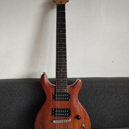 Elektrická kytara s hnědým dřevěným korpusem a tmavým hmatníkem. Na hlavě je viditelné logo "JD". Nástroj má dva černá humbuckery, jeden přepínač a d…