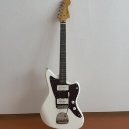 Bílá elektrická kytara s černým pickguardem a hnědým hmatníkem. Na hlavě je viditelné logo Squier. Nástroj má dva snímače, tři ovládací knoflíky a je…