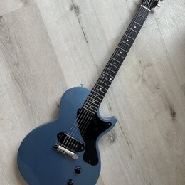 Modře lakovaná elektrická kytara s černým hmatníkem a černým pickguardem. Na hlavě je bílý nápis Gibson a pod ním nápis Les Paul. Nástroj má jeden sn…