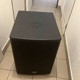 Černý subwoofer s hranatým tvarem a přední textilní maskou. Na horní straně je umístěn kruhový ovládací prvek s několika tlačítky. V dolní části před…