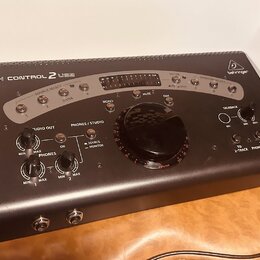 Černý monitorovací kontrolér s bílým rámem a nápisem BEHRINGER v pravém horním rohu. Na předním panelu je uveden model XENYX CONTROL 2 USB a jsou zde…