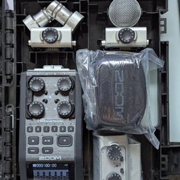 V černém přepravním kufru je umístěn digitální záznamník Zoom H6 Handy Recorder s displejem a ovládacími knoflíky. K němu jsou přiloženy tři stříbrné…