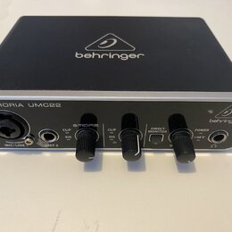 Černý audio rozhraní s hliníkovým stříbrným horním panelem. Na přední straně je nápis U-PHORIA UMC22 a logo behringer, stejně jako na horní části zař…