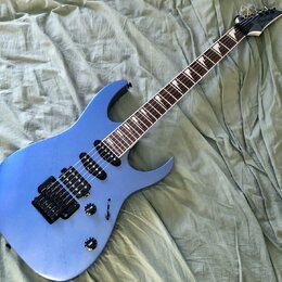 Modrá elektrická kytara s tmavým hmatníkem a černými komponenty. Na hlavě krku je bílý nápis Ibanez. Nástroj má dva humbuckery, jeden ovládací knoflí…