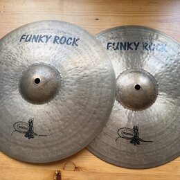 Dvě kovové činely s kovaným povrchem v přirozené barvě. Oba mají nápis FUNKY ROCK a logo s nečitelným textem v dolní části. Na horním činele je drobn…