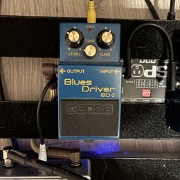 Modrý efekt pedál s nápisy Blues Driver a BD-2. Na spodní části je viditelné logo BOSS. Pedál má tři ovládací knoflíky s popisky LEVEL, TONE a GAIN a…