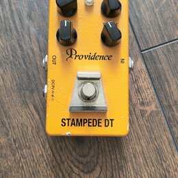 Žlutý kytarový efekt s nápisy Providence a STAMPEDE DT. Na horní straně jsou čtyři černé otočné oválné knoflíky a jeden malý bílý spínač. V dolní čás…