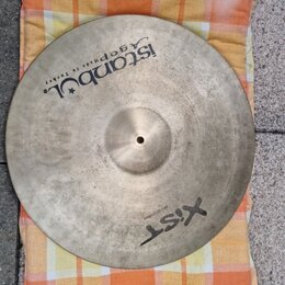 Kruhový činel z kovu s viditelnou strukturou broušení povrchu. Na povrchu jsou černé nápisy „Istanbul Agop Made in Turkey“ a „XIST 20" / 60 cm Ride“.…