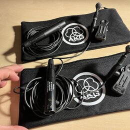 Dvě černé zipové pouzdra s bílým logem AKG. V každém pouzdře je černý mikrofon s připojeným kabelem a držákem. Na spodním mikrofonu je nápis PHANTOM…
