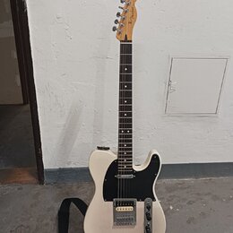 Bílá elektrická kytara s černým pickguardem a hnědým hmatníkem. Na hlavě je viditelné logo Fender. Nástroj má jeden humbucker v pozici mostu a jeden…