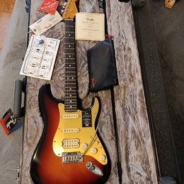 Elektrická kytara typu Stratocaster s barevným přechodem od černé přes červenou k žluté a světlým hmatníkem. Na krytce je nápis „American ULTRA STRAT…