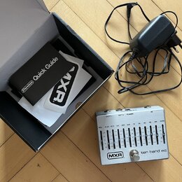 Stříbrný kytarový pedál s nápisy MXR a ten band eq. Na horní straně jsou ovládací posuvníky s označenmi frekvencí od VOL přes 31.25 až po GAIN a kone…