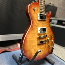 Elektrická kytara s trupem v barvě sunburst a viditnou strukturou dřeva. Nástroj má dva humbuckery s bílými rámečky, čtyři zlaté ovládací knofíky a z…