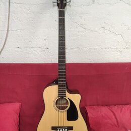 Akustická basová kytara s příměrem v těle, světlým topem a tmavými boky a hmatníkem. Na hlavě je viditelné logo Fender. Nástroj má černý plechtr ochr…
