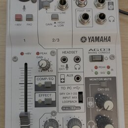 Bílá míchací konzole s nápisem YAMAHA a označením AG03 MIXING CONSOLE. Horní část obsahuje XLR vstup, dva jacky 6,35 mm s nápisy 2G GUITAR a LINE, or…