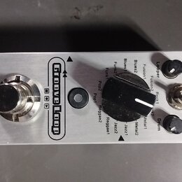 Stříbrný efekt pedál z kovu s nápisy MOOER a Groove Loop. Na horní straně se nachází stoupací spínač, černý oválný volič s popisy stylů (Blues1, Blue…