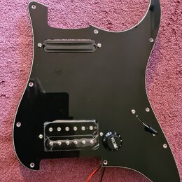 Černý plastový pickguard pro elektrickou kytaru s vyřezem na hmatník a ovládací prvky. Je vybaven jedním černým snímačem v horní části a jedním sníma…
