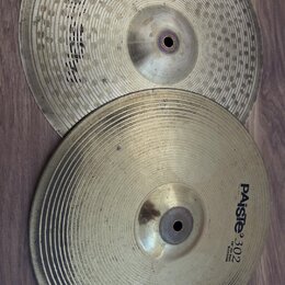 Dvě kovové činely položené na hnědém laminátovém povrchu. Spodní činel má černý nápis PAiste 302 a pod ním menší text 14" HI-HAT Bottom. Horní činel…