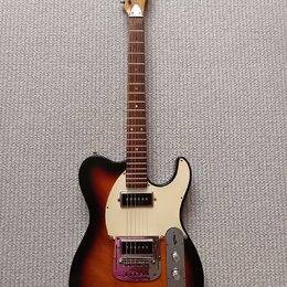 Elektrická kytara typu Telecaster s tělem v provedení sunburst a bílým pickguardem. Na hlavě hředu je vidět nápis "Aria". Kytara má dva snímače, kovo…