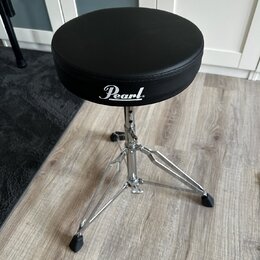 Černý bubeníckýstolek s kulatým polstrovaným sedadlem a chromovanou třínohou základnou. Na boku sedadla je bílý nápis Pearl. Povrch sedadla i chromov…