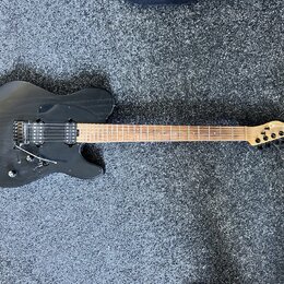 Černá elektrická kytara s hnědým hnedým hradlem a světlou barvou dřeva na hlavě. Na hlavě je viditelné logo OK. Kytara má dva humbuckery, tremolo mec…