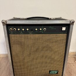Kytarový kombo zesilovač v hliníkovém flightcase s černou rukojetí a kovovými rohy. Horní ovládací panel je zelený s bílými nápisy INPUTS, VOLUME, ov…