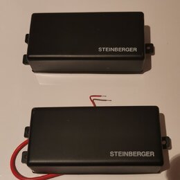 Dvě černé obdélníkové krabičky s nápisem STEINBERGER. Spodní kus má připojený červený kabel. Povrch je matný a v dobrém stavu.