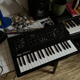Černý syntetizátor s klaviaturou umístěný na podstavci. Na levé straně panelu je bílý nápis KORG minilogue xd a pod ním menší text POLYPHONIC HYBRID…