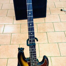 Elektrická basová kytara s korpusem v přechodovém žlutomodrém odstínu (sunburst) a tmavým hmatníkem. Na hlavě je viditelné logo "Fender". Kytara má č…