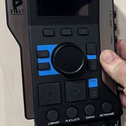 Černý elektronický přístroj s displejem a ovládacími prvky. Na levé straně je bílé logo s písmenem B a nápisem BEAT. Na spodní části jsou tlačítka s…
