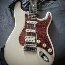 Bílá elektrická kytara s hnědým vzorovaným pickguardem. Na spodním snímači je viditelný nápis Seymour Duncan. Kytara vykazuje známky opotřebení v pod…