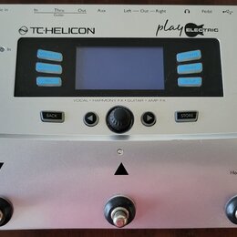 Stříbrný efektový procesor s nápisy TC-HELICON a play ELECTRIC. Zařízení má centrální displej, modrá tlačítka s popisky VOCAL FX, GUITAR FX, MIX, FAV…
