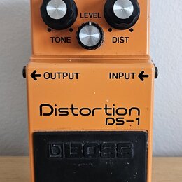 Oranžový kytarový efekt s nápisy Distortion a DS-1. Na horní části jsou tři ovládací knoflíky s popisky TONE, LEVEL a DIST a červená kontrolka CHECK.…