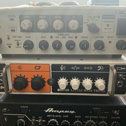 Fotografie zachycuje tři zesilovače naskládané na sebe. Horní je šedý s nápisy KATANA 500 BASS HEAD a BOSS POWER. Prostřední je bílý s oranžovým pane…