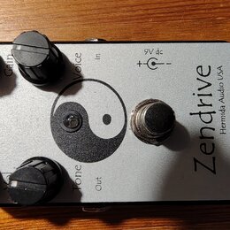 Stříbrný kytarový efekt s nápisem Zendrive a menším textem Hermida Audio USA. Na horní straně jsou čtyři černé otočné knoflíky s popisky Gain, Voice…