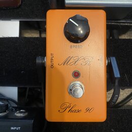 Oranžový efekt pedál s černým ovládacím knoflíkem a stříbrným spínacím tlačítkem. Na povrchu jsou nápisy SPEED, OUTPUT, INPUT, logo MXR a model Phase…