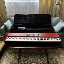 Červený digitální klavír s bílými a černými klávesami. Na pravé straně korpusu je bílý nápis nord piano. Nástroj leží na hnědém dřevěném stole před o…