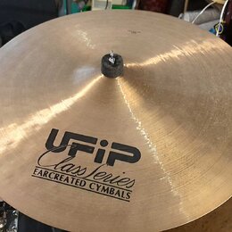 Zlatavý kovový činel s černým logem a nápisy UFIP, Class Series a EARCREATED CYMBALS. V centru je umístěna černá plstěná podložka s kovovým šroubem.…