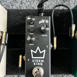 Černý efekt pedál s nápisy „aguiar“, „GAIN“, „KICK“, „MASTER“ a „SHAPE“. Ve spodní části je bílé logo ve tvaru koruny a text „STORM KING“. Pedál má t…