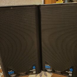Dvě černé reproduktorové bedny s kovovou mřížkou. Na spodní části jsou viditelné nápisy K12.2, 2000 WATT a logo QSC s označením K.2 SERIES. Dále je z…