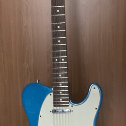 Modrá elektrická kytara typu Telecaster s bílým pickguardem a hnědým hmatníkem. Na hlavě krku je viditelné logo Fender. Nástroj vykazuje známky běžné…