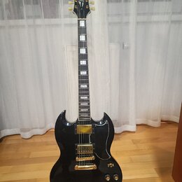 Černá elektrická kytara s dvojstupňovitým tělem a hnědým hmatníkem s trapezoidními vložkami. Na hlavě je bílý nápis Epiphone a zlaté loga. Nástroj má…
