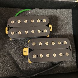Dvě elektrické kytarové snímače typu humbucker s černými kryty. Snímače jsou umístěny na šedé pěnové výplasti v krabici. Na snímačích nejsou viditeln…
