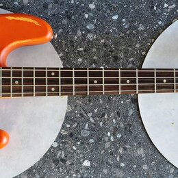 Oranžová elektrická basová kytara s červeným perleťovým pickguardem. Na hlavě hmatníku je nápis Vintage ICON Series. Povrch těla vykazuje výrazné odř…