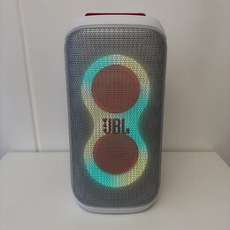 Bílý přenosný reproduktor s šedou kovovou mřížkou. Uprostřed je umístěno podsvícené logo JBL a dvě kulaté svítící plochy. Horní část reproduktoru je…
