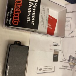 Na fotografii je černý obdélníkový modul s nápisem Seymour Duncan a doprovodný papírový návod se schématem zapojení. Modul je umístěn vedle průhledné…