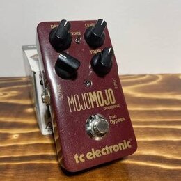 Vínový efekt pedál s kovovým povrchem a čtyřmi černými ovládacími knoflíky. Na přední straně jsou bílé nápisy VOICE, LEVEL, DRIVE a TONE u knoflíků,…