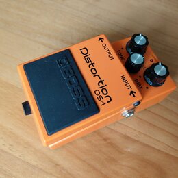Oranžový efekt pedál s černým gumovým spínacím tlačítkem, na kterém je vyražený nápis BOSS. Na horní části je uveden název Distortion DS-1 a popisky…
