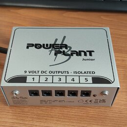 Stříbrný kovový napájecí adaptér s nápisem POWER PLANT Junior. Na horní straně je text 9 VOLT DC OUTPUTS - ISOLATED a čísla 1 až 5 nad odpovídajícími…